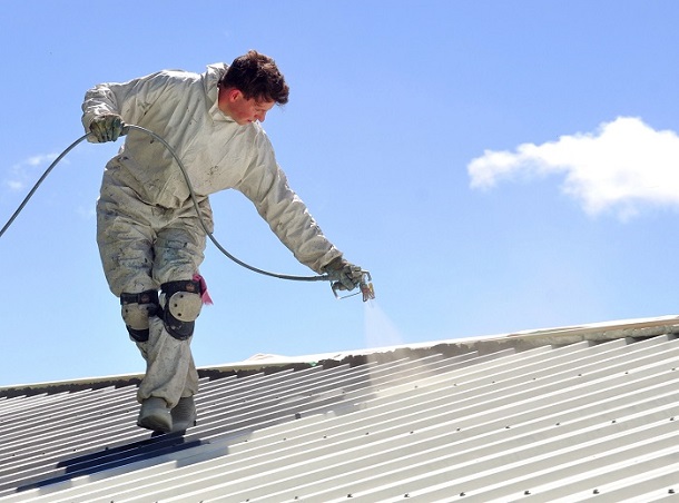 17277902 - a trademan uses an airless spray to paint the roof of a building